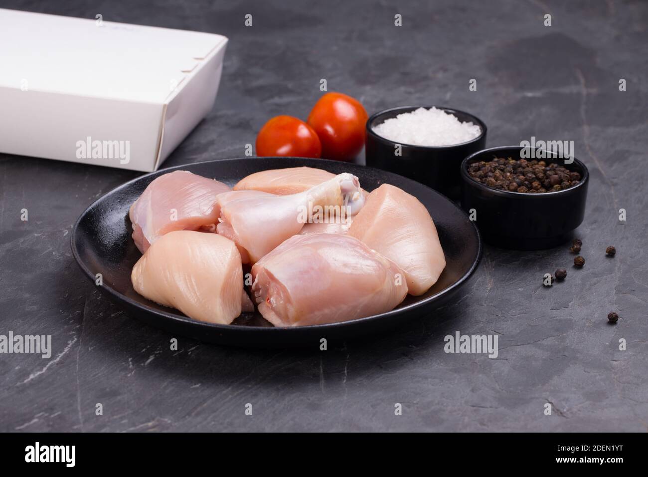 Pollo crudo tenero curry tagliato senza pelle disposto su nero piastra con ingredienti da cucina su sfondo bianco con scatola per la consegna nelle vicinanze Foto Stock