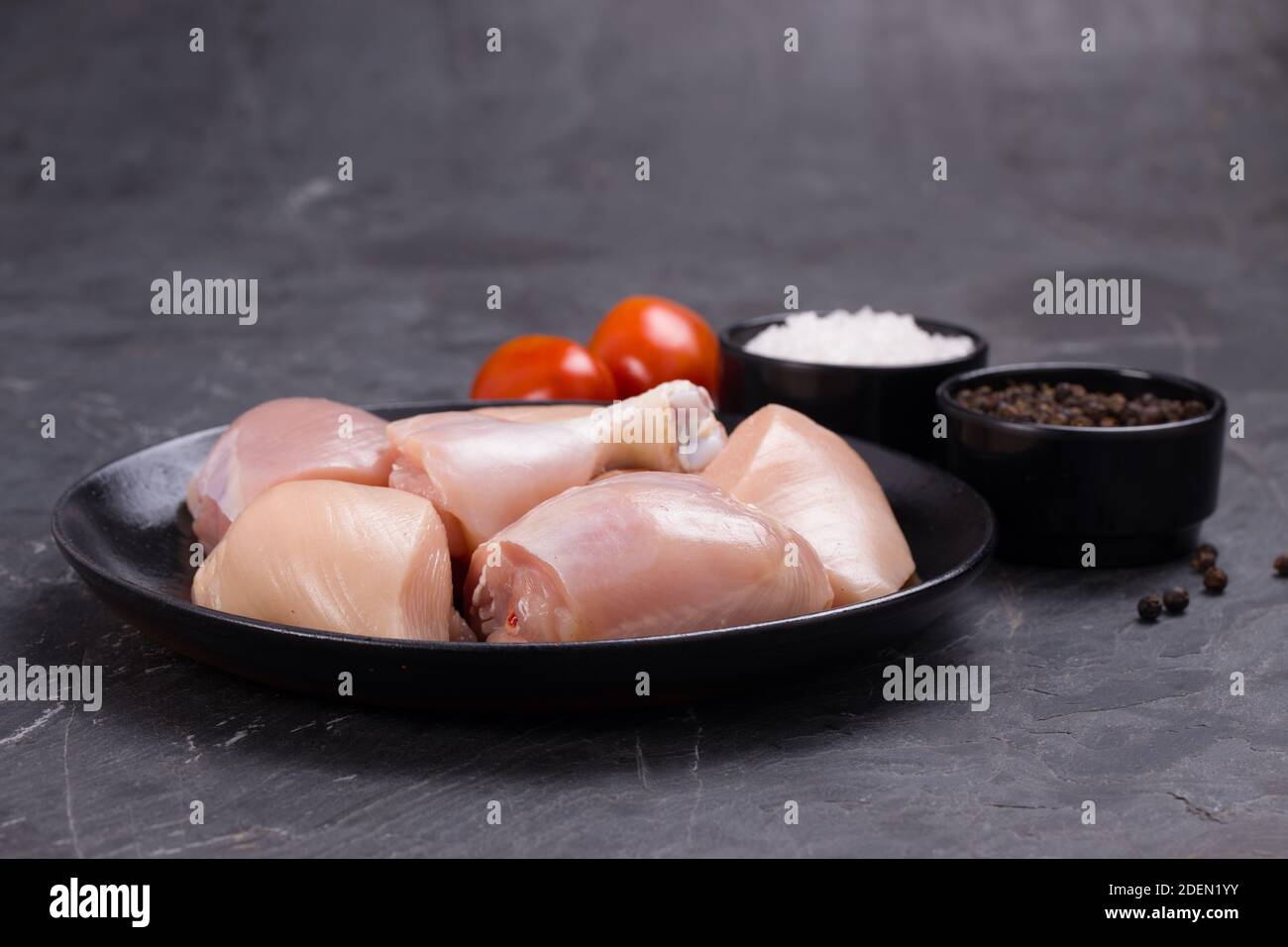 Pollo crudo tenero curry tagliato senza pelle disposto su nero piastra con ingredienti per la cottura su sfondo bianco Foto Stock