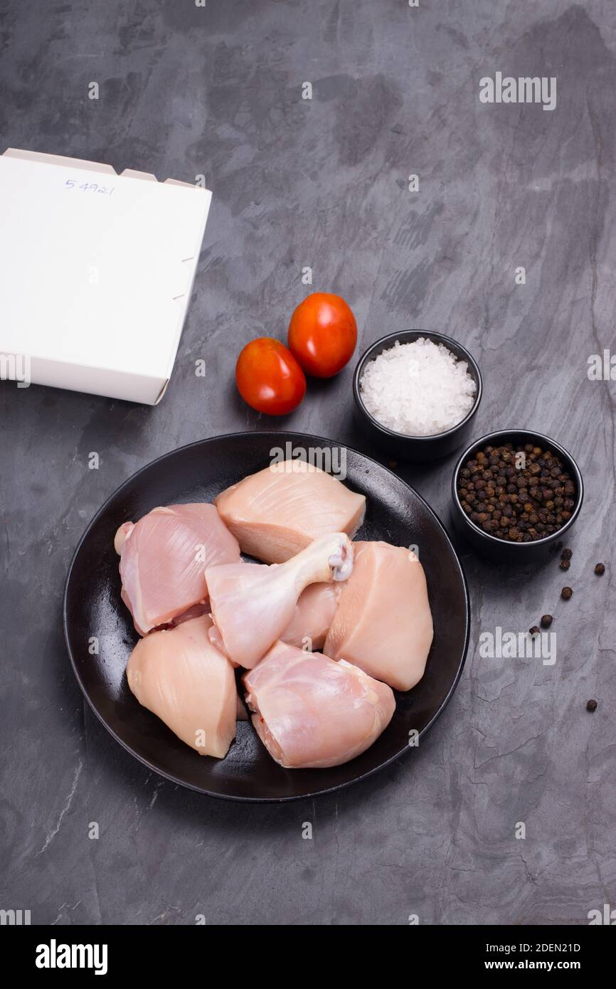 Pollo crudo tenero curry tagliato senza pelle disposto su nero piastra con ingredienti da cucina su sfondo bianco con scatola per la consegna nelle vicinanze Foto Stock