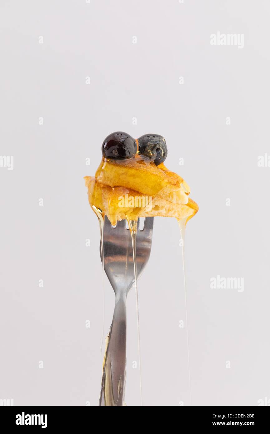 Primo piano di pancake e frutti di bosco con miele gocciolante forchetta su sfondo bianco Foto Stock