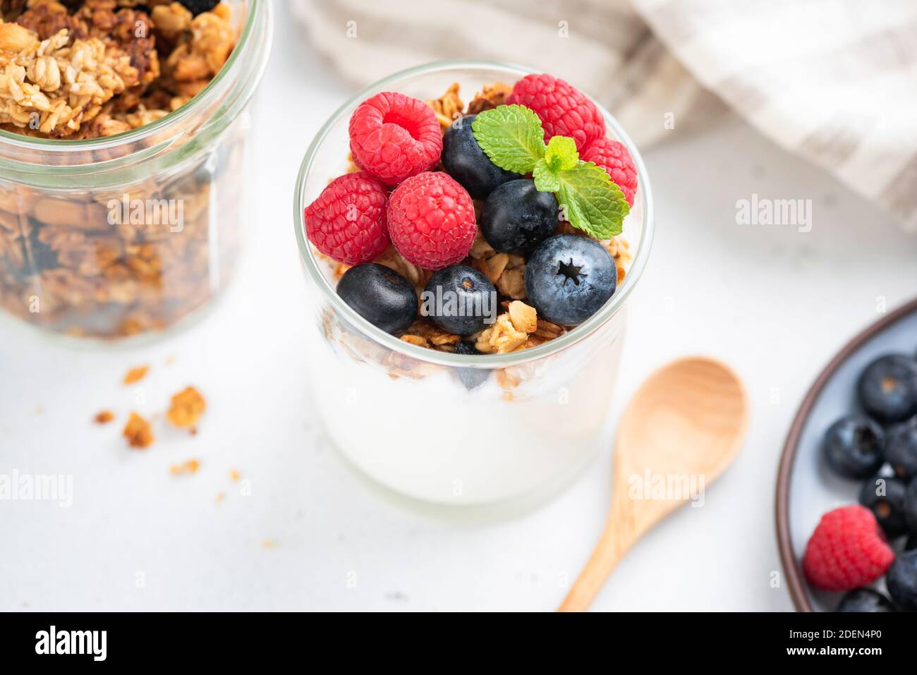 Yogurt con frutti di bosco e muesli in vaso su tavola bianca. Cibo pulito, dieta, concetto di cibo sano Foto Stock