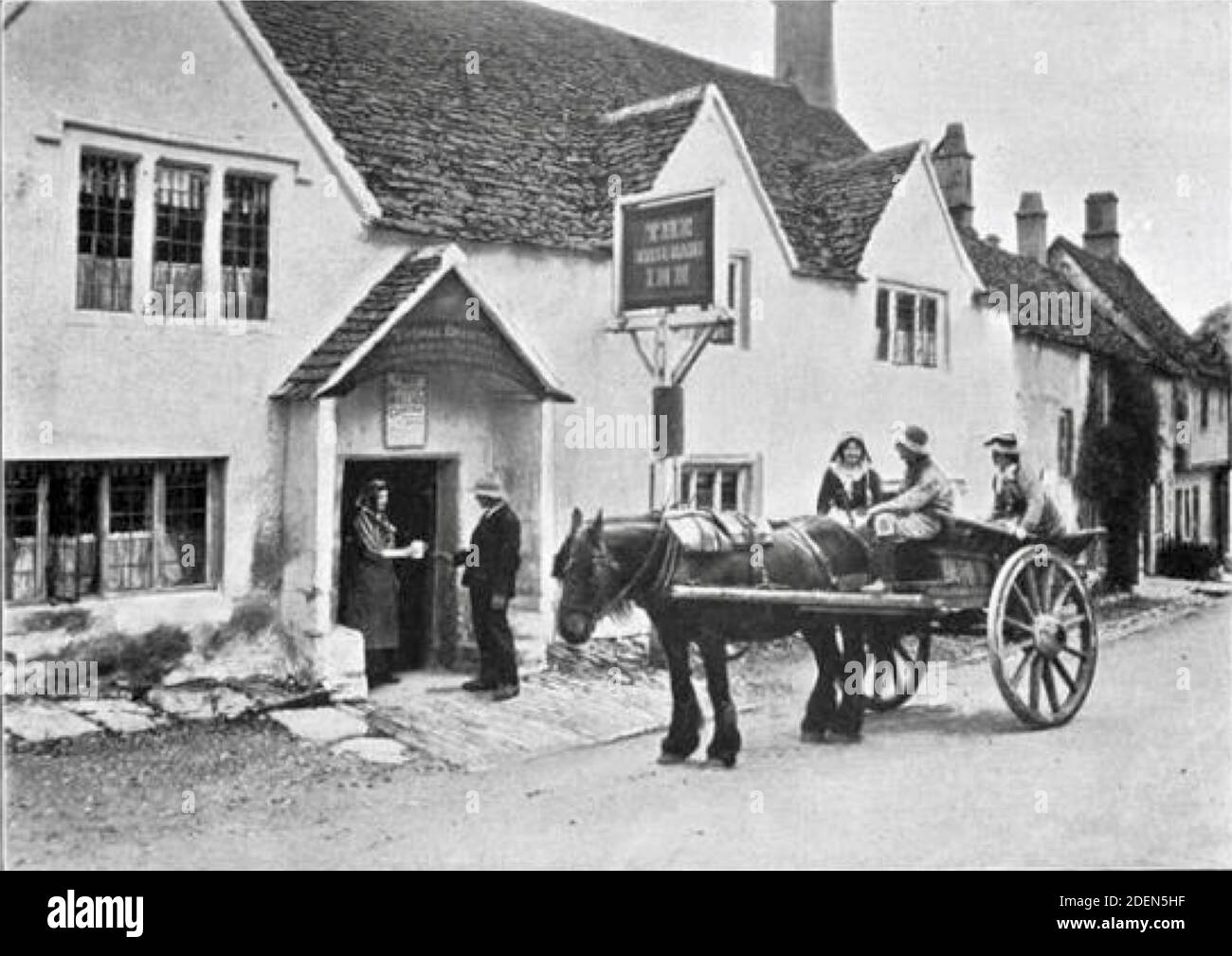 Vecchia fotografia di Graystone Bird del White Hart Inn, Castle Combe, Wiltshire. Una tazza di sidro è servita fuori dal pub come un carro e un cavallo in attesa. Foto Stock