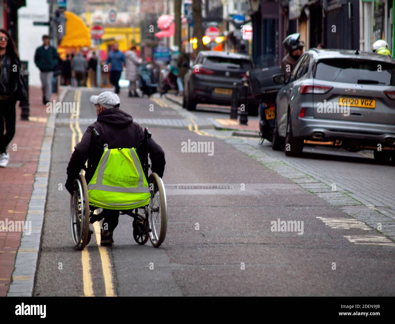 Un utente in sedia a rotelle scende lungo una strada a Brighton Foto Stock