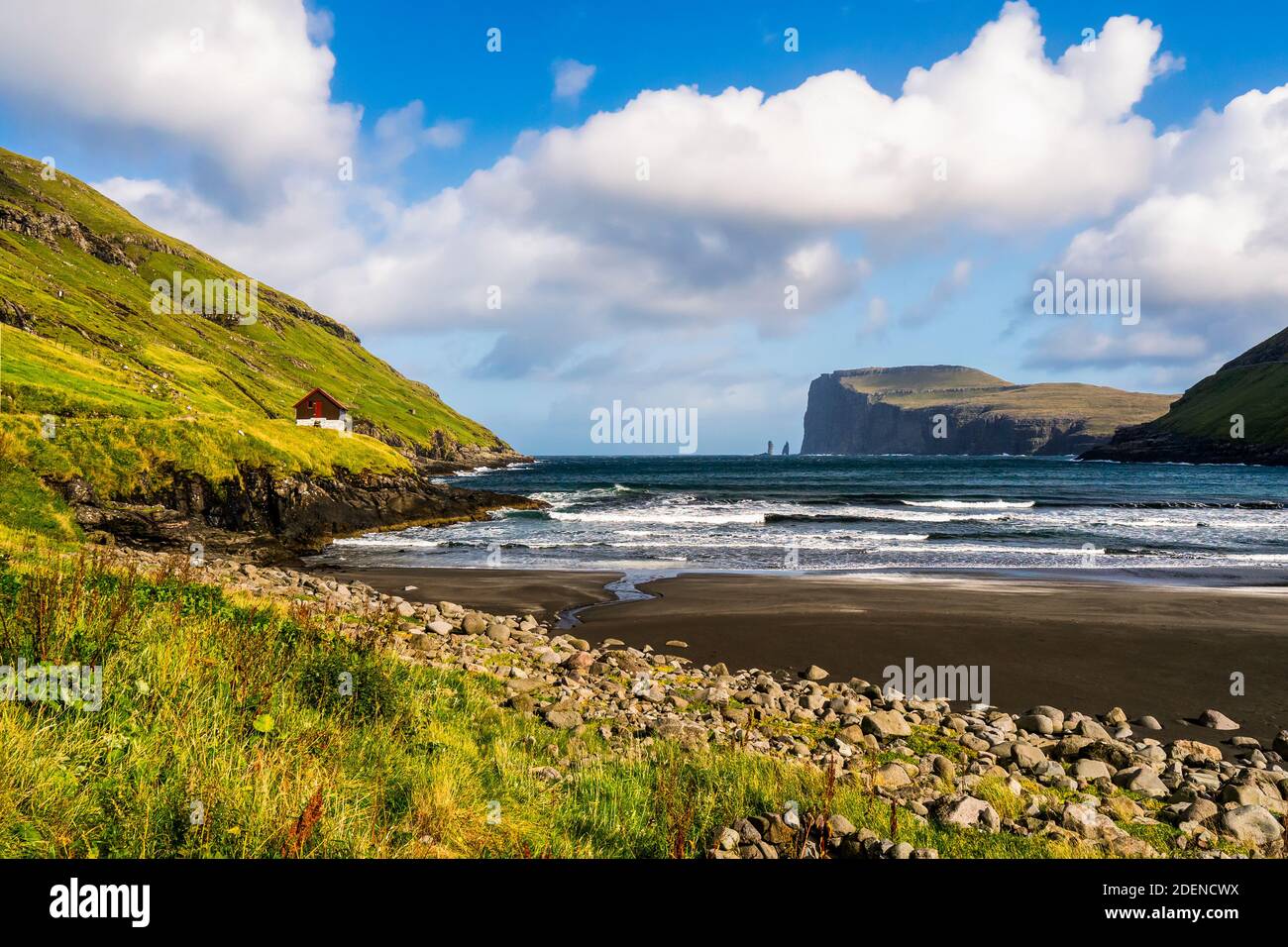 Spiaggia nera e mare ruvido circondato da montagne erbose nella costa Vidareidi sull'isola di Vidoy, l'isola di Faroe. Paesaggio soleggiato del villaggio faroese Foto Stock