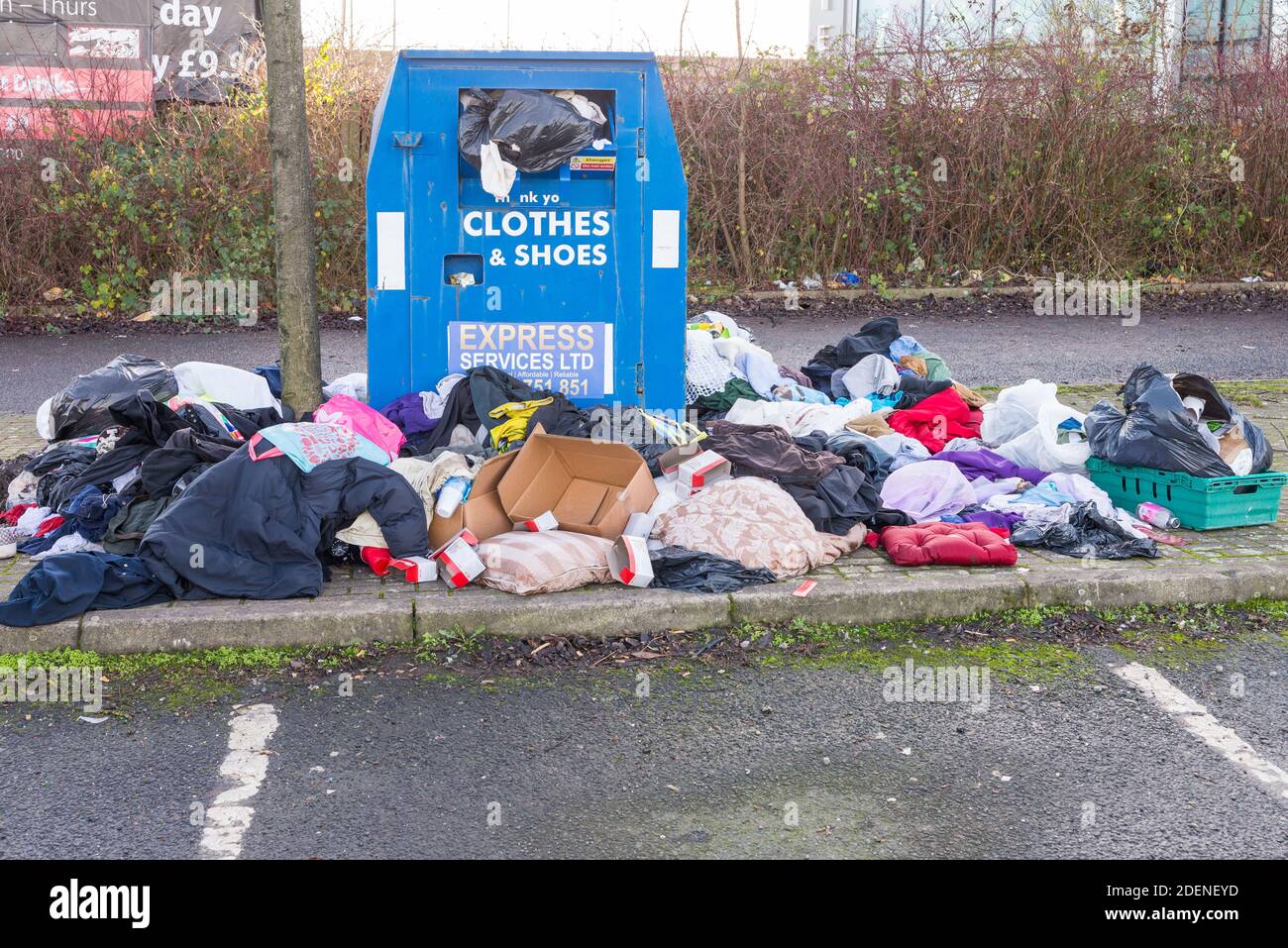 Indumenti e scarpe traboccanti riciclare unità di raccolta beneficenza con abiti sparsi intorno ad esso Foto Stock