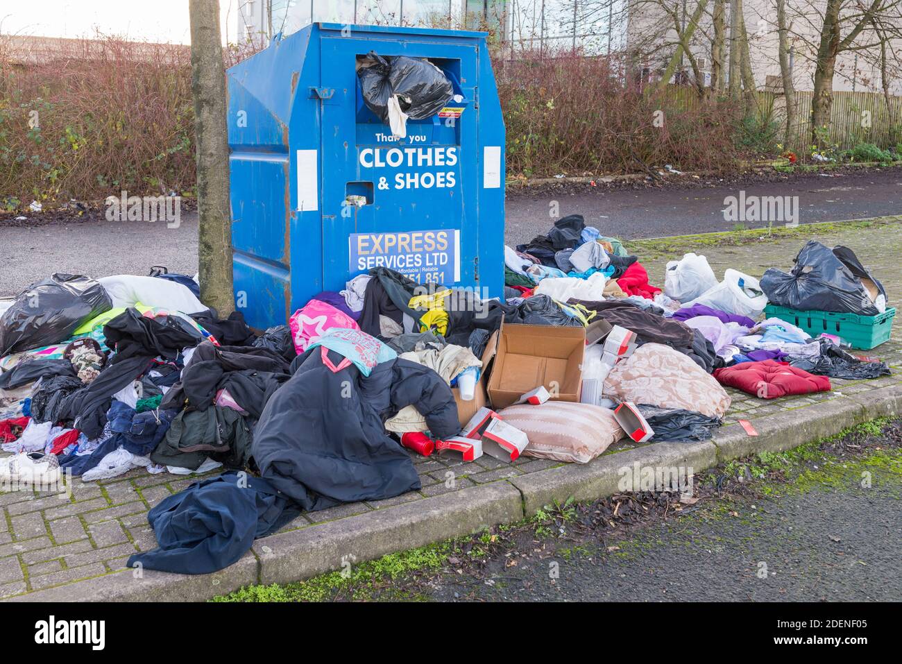 Indumenti e scarpe traboccanti riciclare unità di raccolta beneficenza con abiti sparsi intorno ad esso Foto Stock