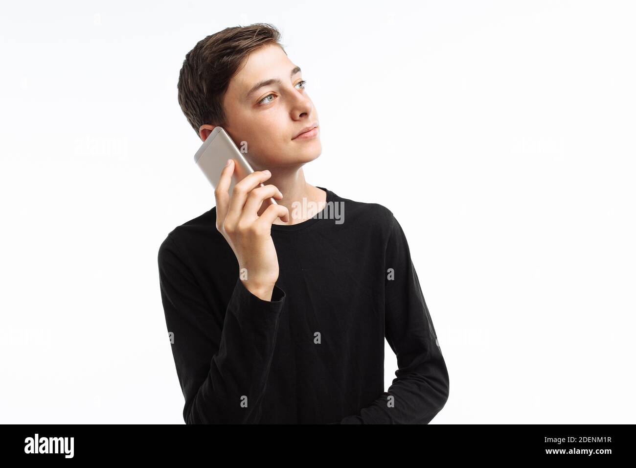 Ritratto di un adolescente emozionale, che parla al telefono, in una t-shirt nera, su sfondo bianco, Foto Stock