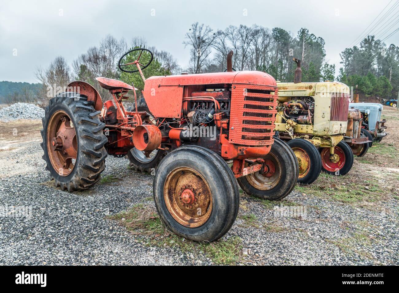 Una fila di vecchi trattori di fattoria d'epoca parcheggiata in un campo di ghiaia non più utilizzato per decadere all'aperto Foto Stock