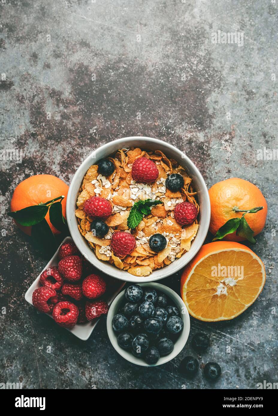 Colazione sana. Ciotola con cereali, lamponi e mirtilli accanto alle arance su fondo grunge Foto Stock