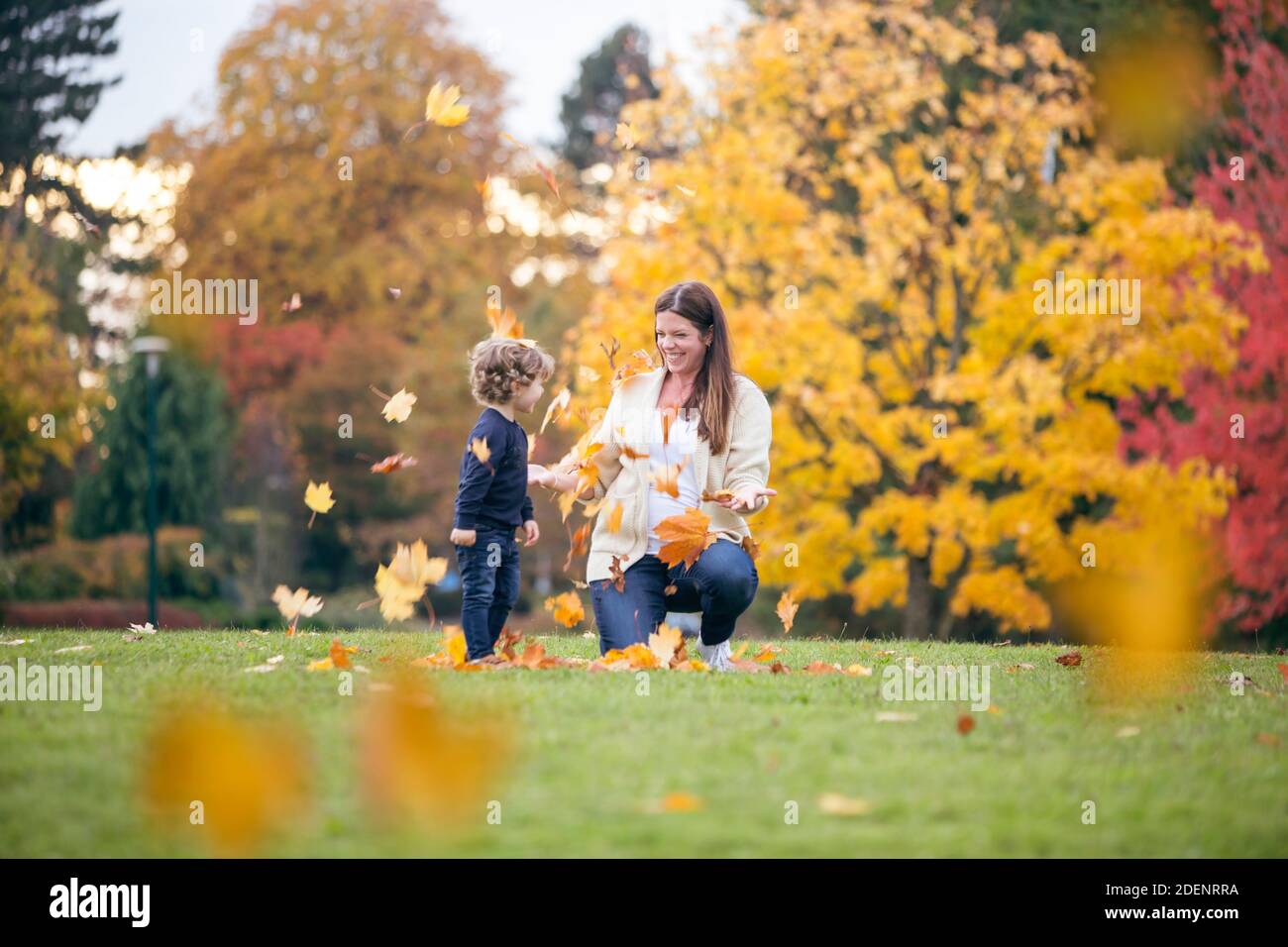 Una giovane madre e suo figlio giocano nel parcheggia contro splendidi colori autunnali che illustrano la felicità e la gioia di famiglia Foto Stock