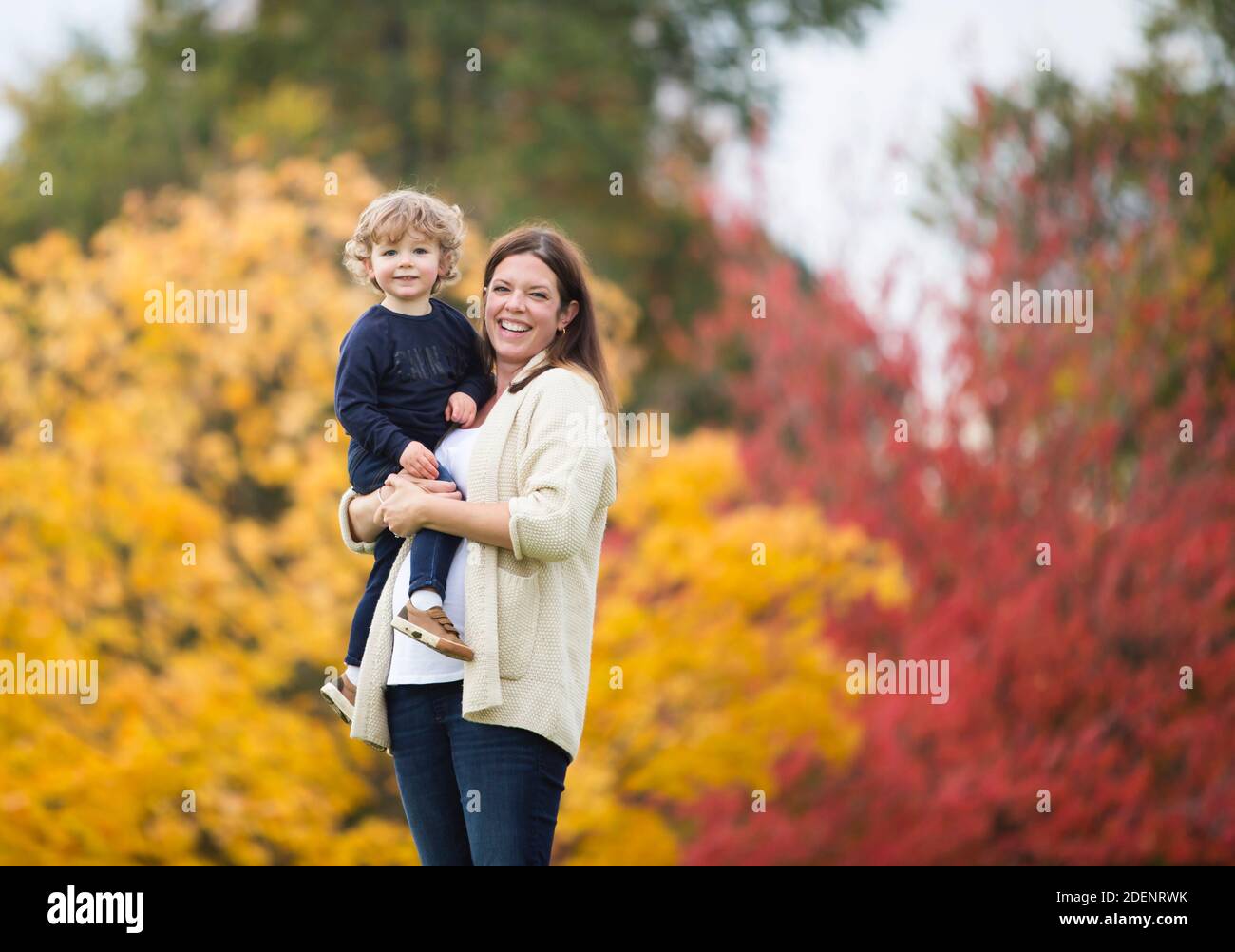 Una giovane madre e suo figlio giocano nel parcheggia contro splendidi colori autunnali che illustrano la felicità e la gioia di famiglia Foto Stock