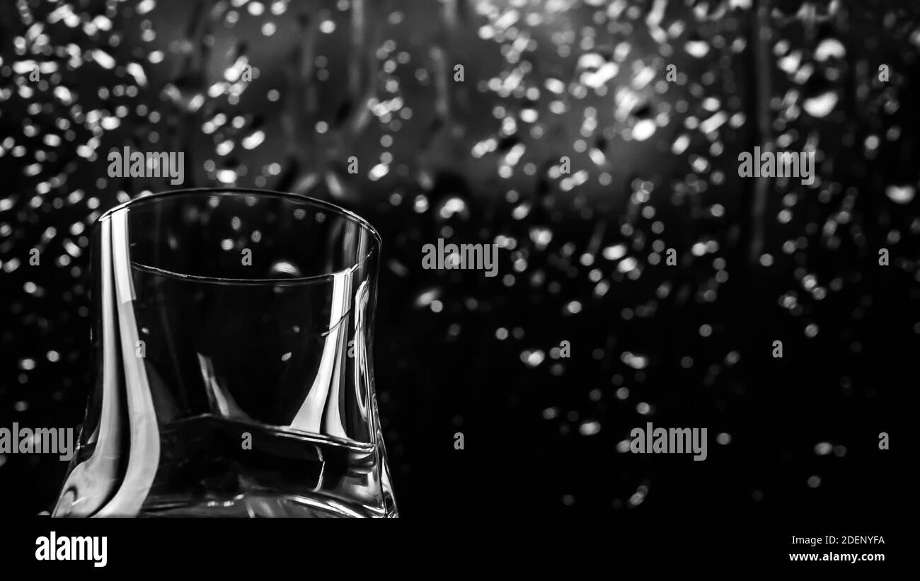 Sfondo di pioggia con alcol, whisky in un bicchiere su sfondo nero, gocce di pioggia scorrono lungo il bicchiere Foto Stock