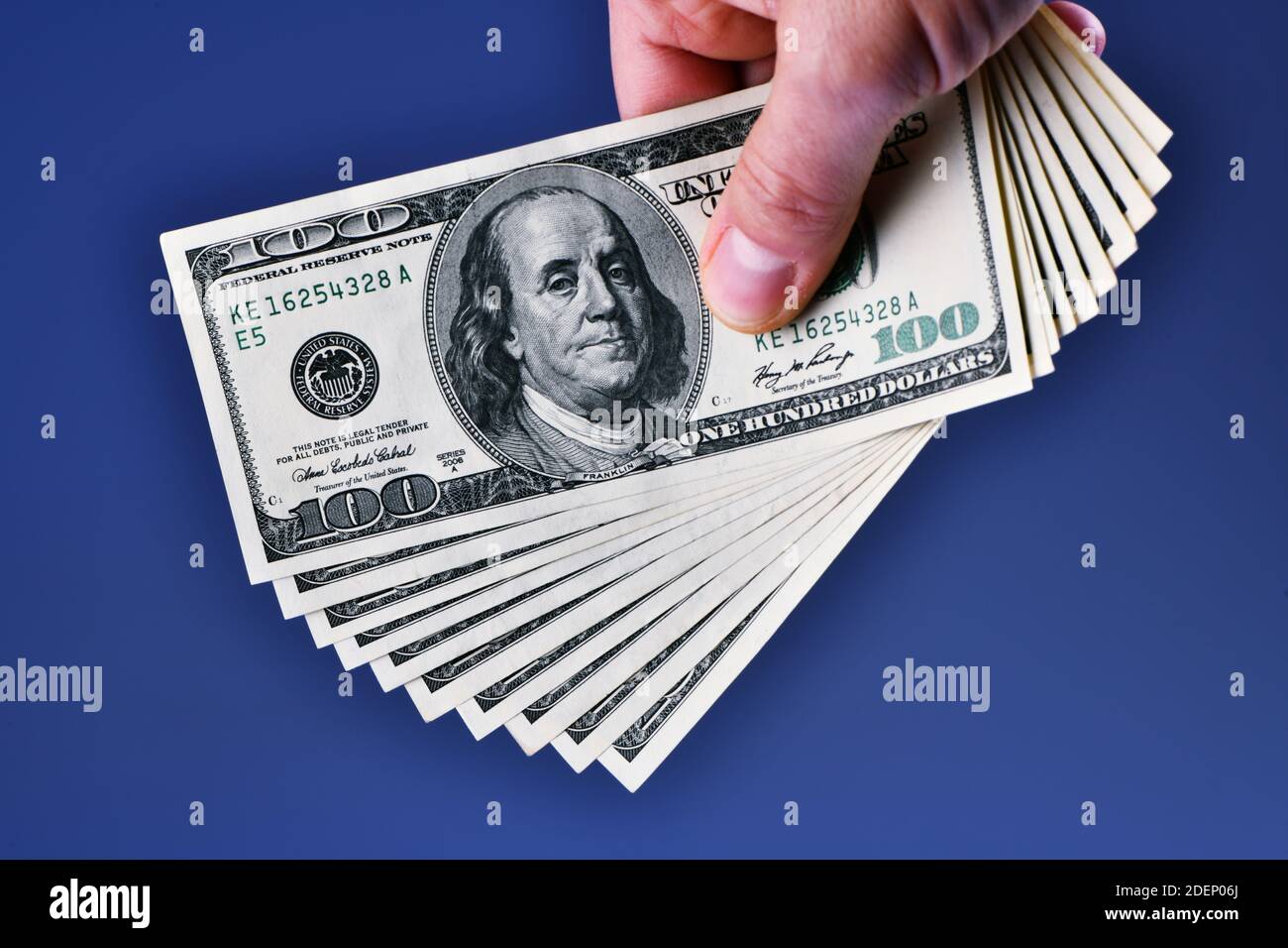 Una mano dell'uomo isolata su uno sfondo blu mostra una mazzo di 1000 dollari in dieci 100 dollari fatture Foto Stock