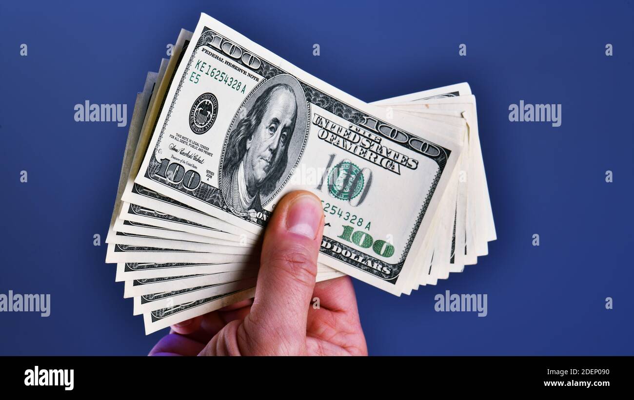 Una mano dell'uomo isolata su uno sfondo blu mostra una mazzo di 1000 dollari in dieci 100 dollari fatture Foto Stock