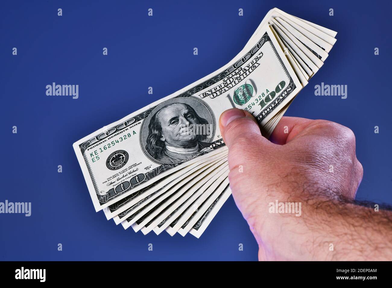 Una mano dell'uomo isolata su uno sfondo blu mostra una mazzo di 1000 dollari in dieci 100 dollari fatture Foto Stock