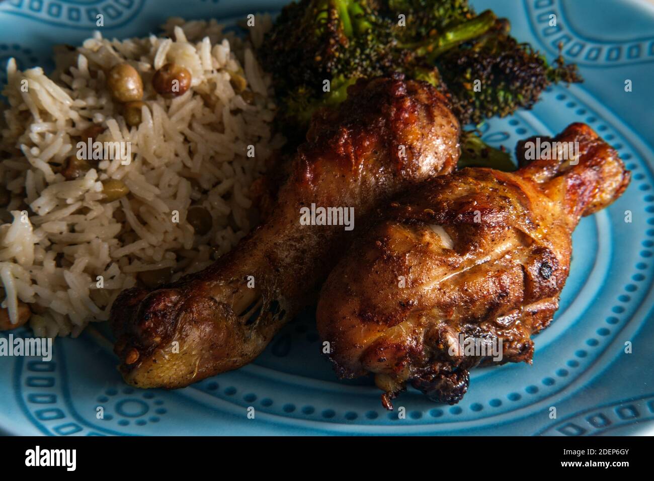 Autentiche e speziate gambe di pollo giamaicano a jerk servite con riso al cocco e piselli di piccione Foto Stock