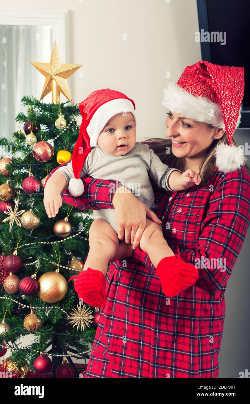 Madre e il suo bel bambino che posano accanto all'albero di Christmass con cappelli babbo natale Foto Stock