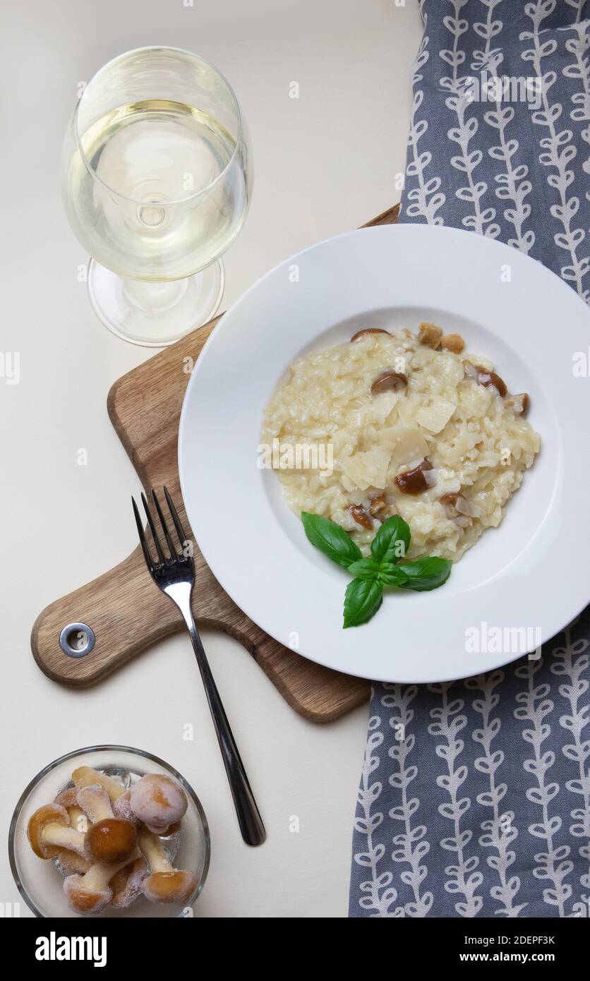 Risotto vegetariano gourmet di funghi su un piatto bianco, sfondo giallo, servito con un bicchiere di vino bianco. Un piatto di riso dell'Italia settentrionale cotto con brodo fino a raggiungere una consistenza cremosa. Foto Stock