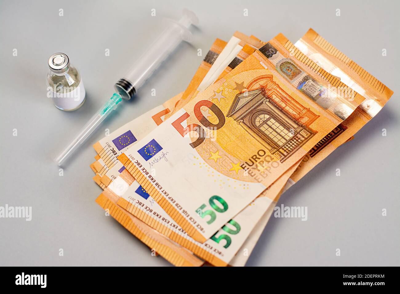 Una pila di soldi e vaccino, medicina e siringa su sfondo grigio Foto Stock