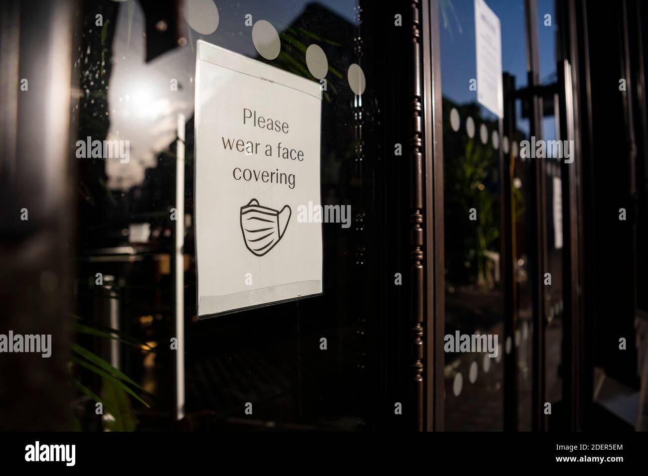 Il cartello informativo del Coronavirus Covid-19 dice prego di indossare una maschera di copertura in una vetrina mentre i negozi sono stati chiusi durante il blocco a Londra su una strada vuota shopping in Inghilterra, Europa Foto Stock
