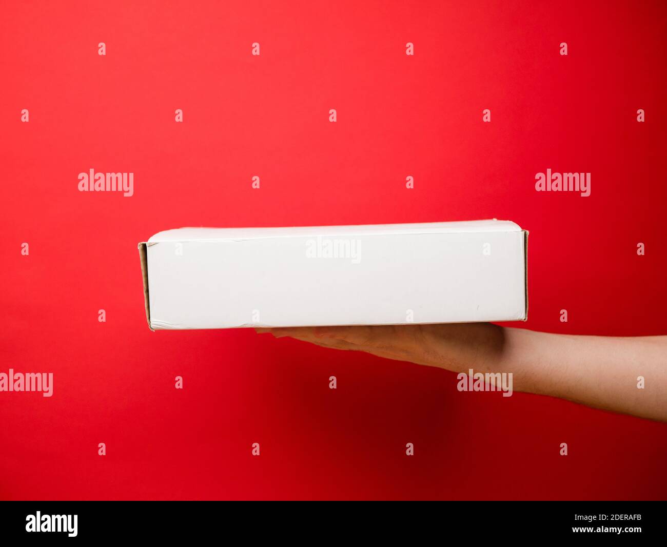 Scatola sulla mano maschio. Spedizione di cibo. Servizio di consegna veloce. Stile di mockup e spazio di copia. Concetto di cartone. Isolato in rosso. Foto Stock