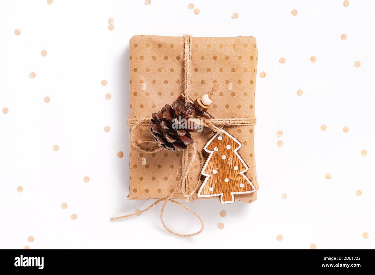 Accogliente confezione regalo avvolta in carta artigianale con Natale in legno decorazioni ad albero su sfondo bianco con confetti Foto Stock