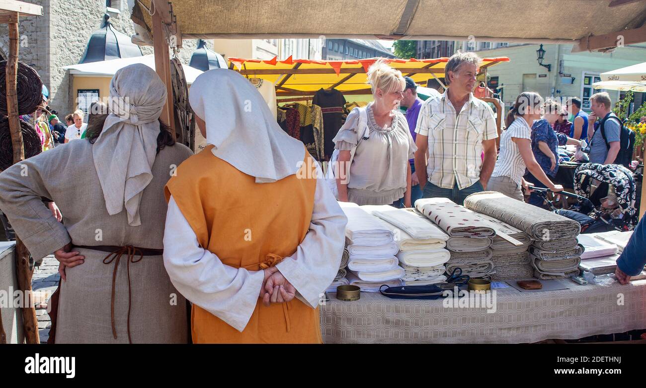 Le donne in abito medievale vendono tessuti da una stalla nella piazza centrale di Tallinn, Estonia Foto Stock