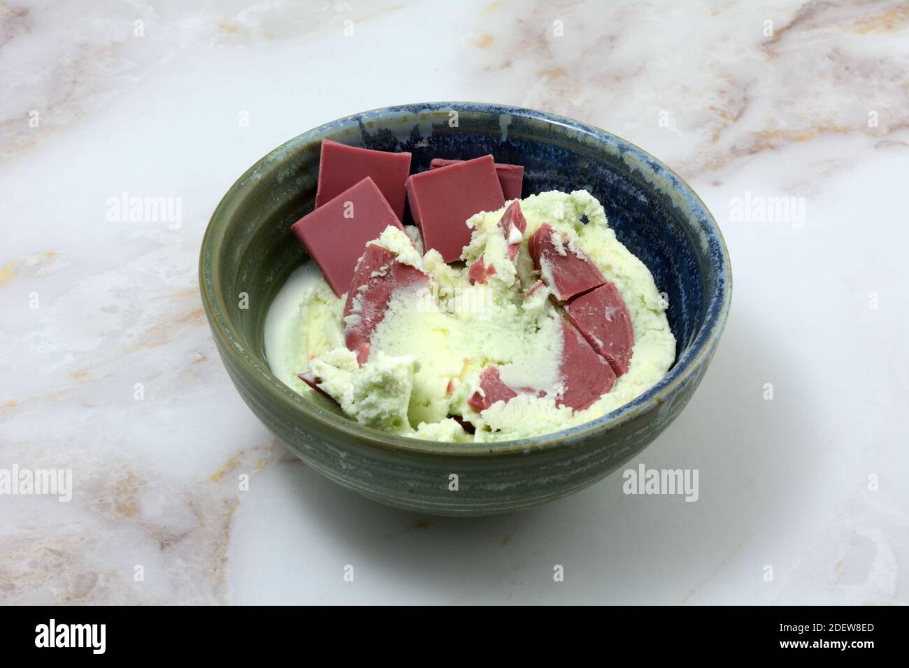 Crema dolce al pistacchio a strati e gelato al cioccolato al rubino con caramelle al cioccolato al rubino sul lato nel recipiente in ceramica tabella Foto Stock