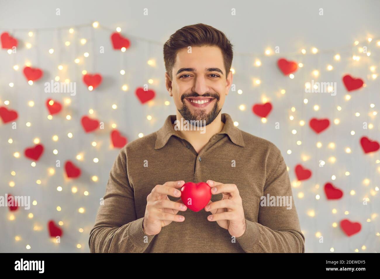 Ritratto di un giovane sorridente che tiene un piccolo cuore rosso di San Valentino e guardando la fotocamera Foto Stock