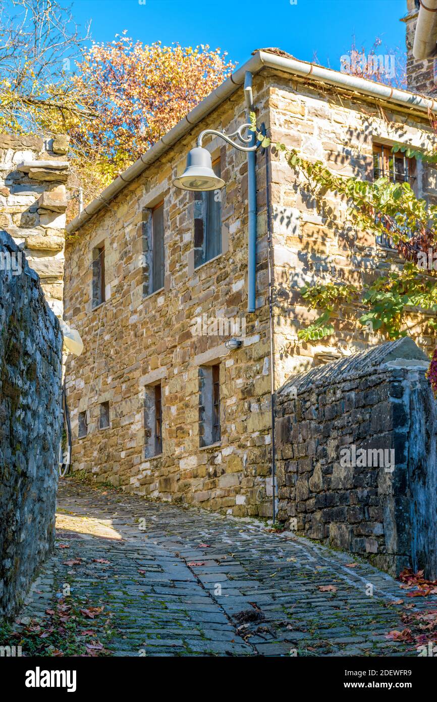Architettura tradizionale con una stretta strada in pietra e la montagna astraka AS Contesto durante la stagione autunnale nel villaggio di Papigo a zagori Grecia Foto Stock