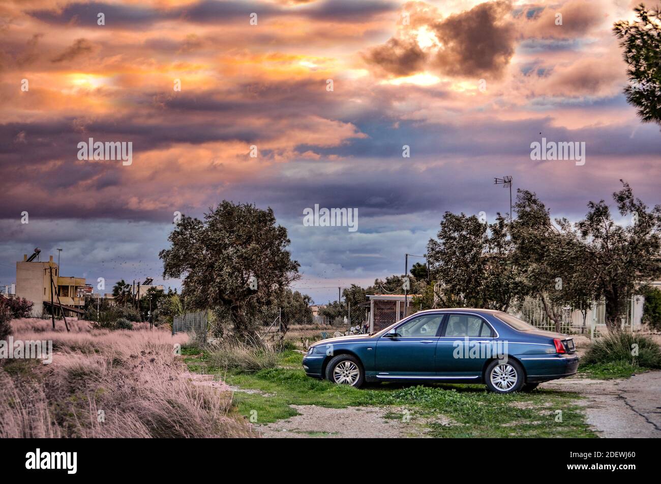 Una bella auto blu degli anni '90 sotto un cielo drammatico al tramonto Foto Stock