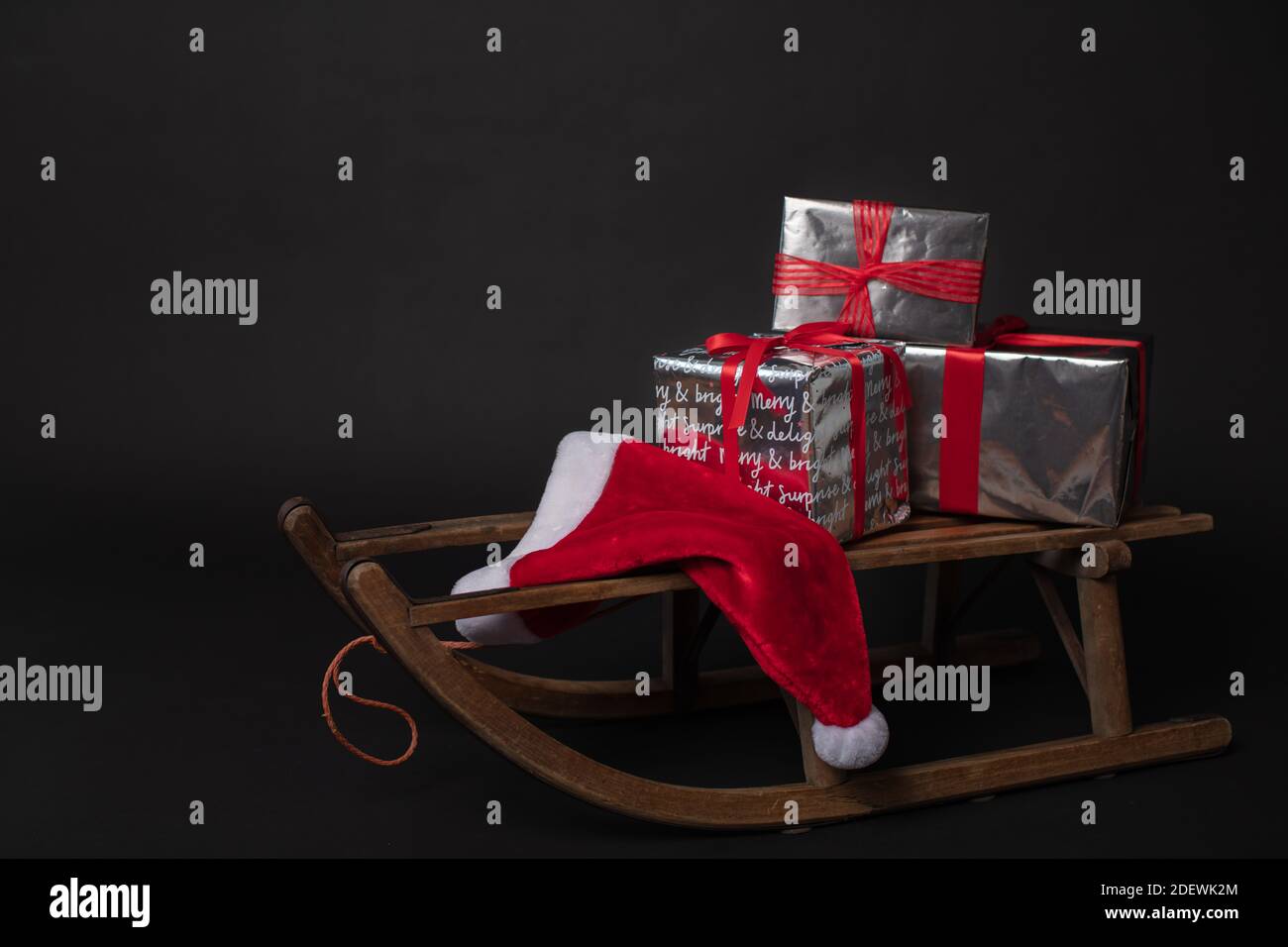 Slitta rustica con scatole regalo e cappello Santas accanto Alberi di Natale Foto Stock