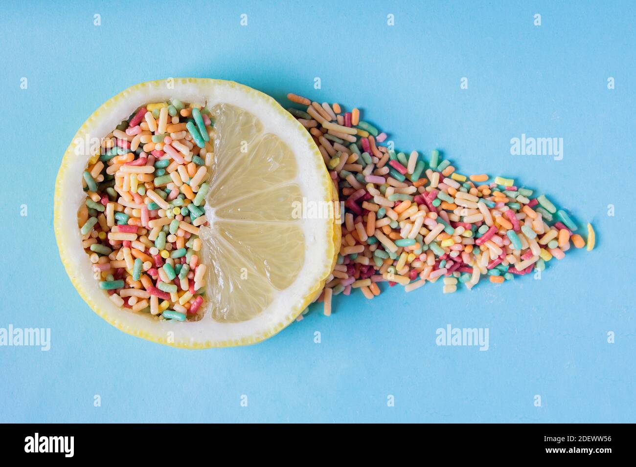 Una fetta di limone piena di polpa e dolci lascia una traccia di caramelle colorate su uno sfondo blu pastello. Zucchero e frutta nei dessert. Foto Stock