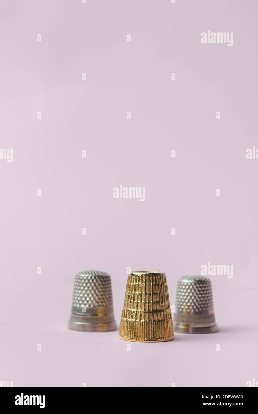 Immagine verticale di una composizione triangolare di tre thimbles, due tipi, e un oro su sfondo rosa. Articoli da cucire. Foto Stock
