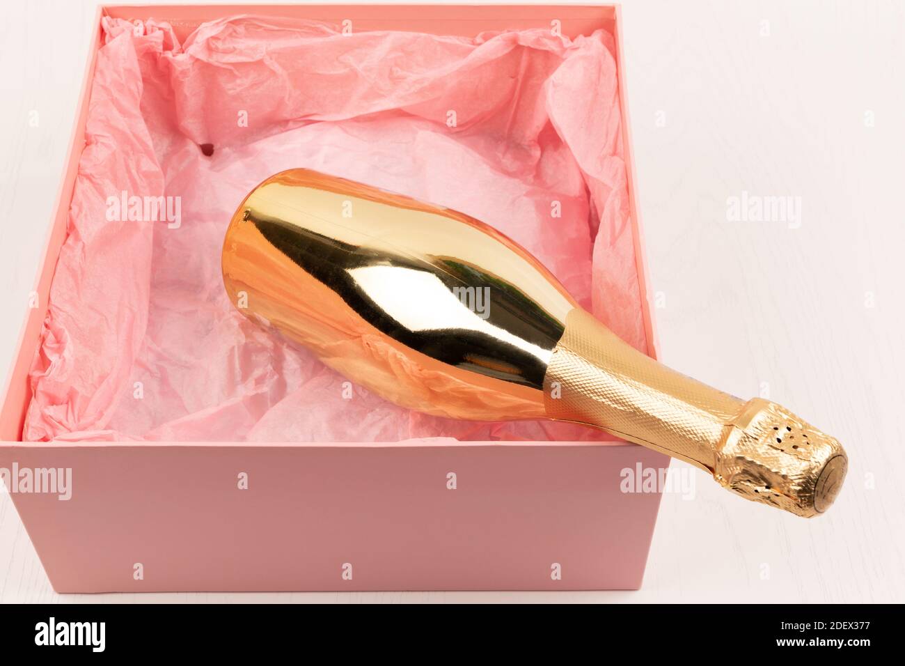 una bottiglia d'oro di champagne si trova in una scatola rosa regalo su uno sfondo bianco tavolo di legno Foto Stock