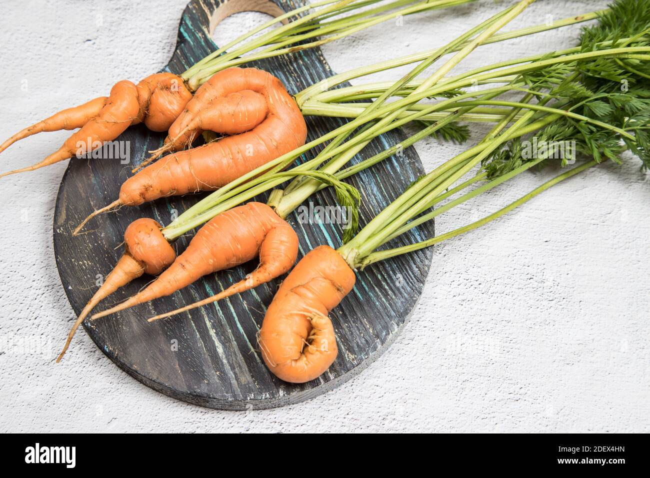 Cinque radici di carota brutto su una tavola rotonda di legno. Foto Stock