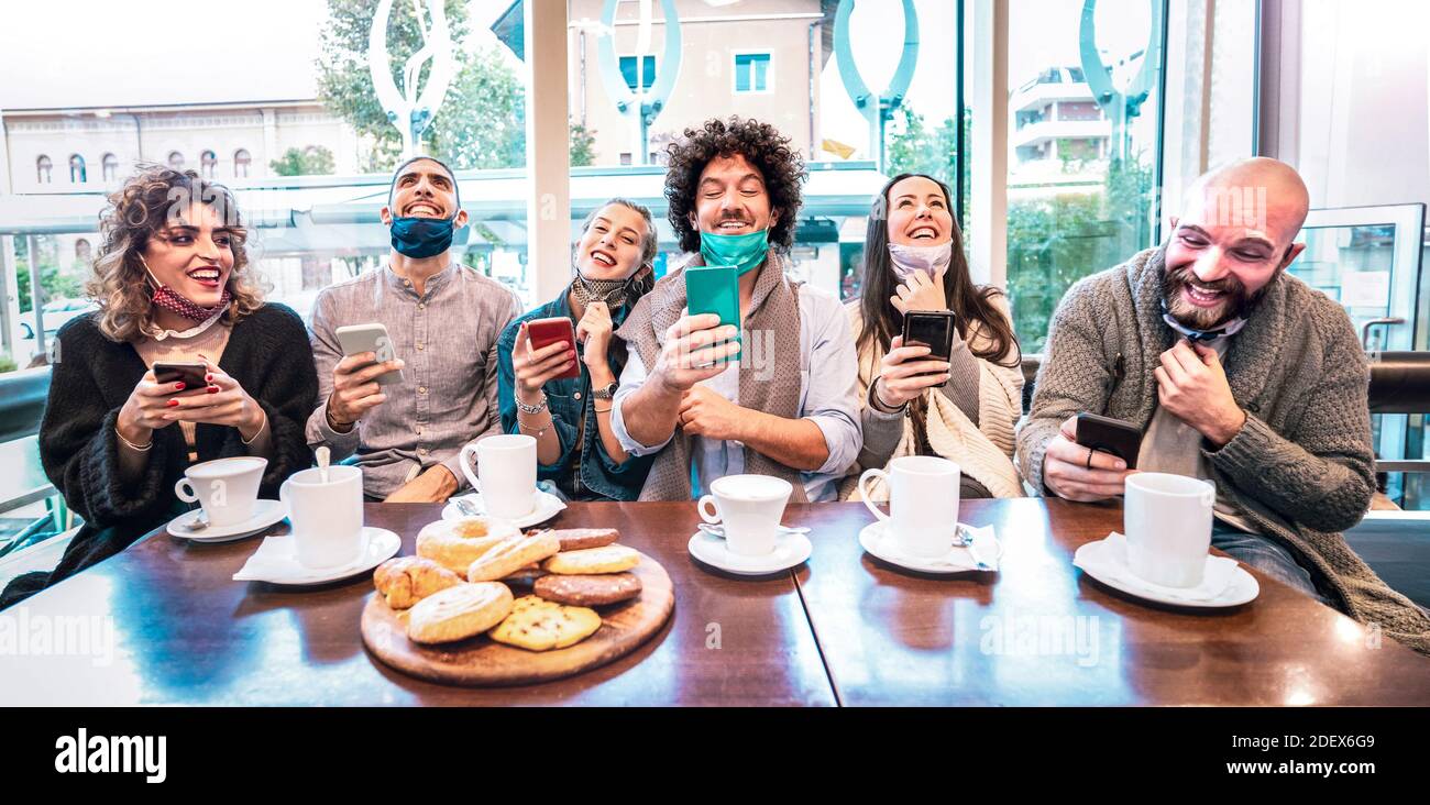 Amici felici che usano gli smartphone al bar del caffè - Nuovo concetto di stile di vita normale con le persone che indossano una maschera facciale aperta e guardare video divertenti Foto Stock