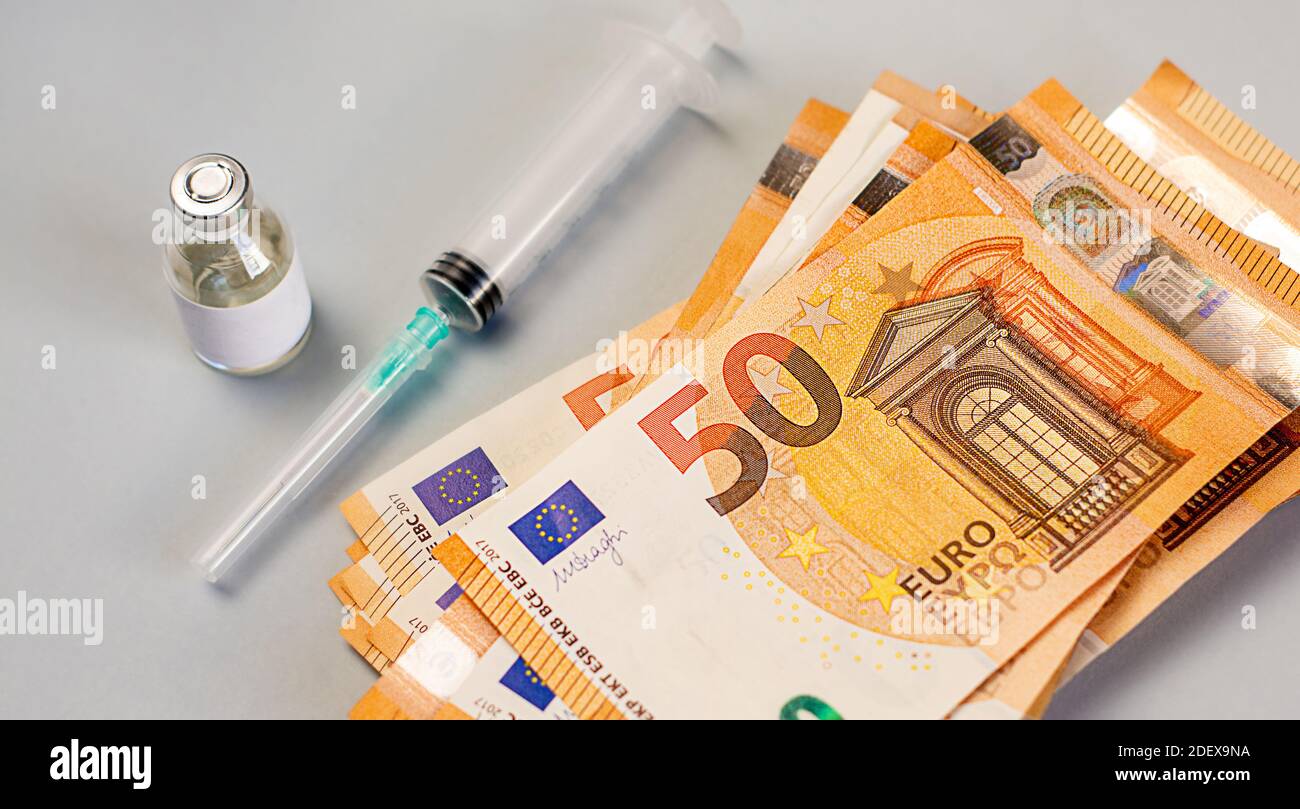 Una pila di soldi si trova vicino a un vaccino, una medicina e una siringa su uno sfondo grigio Foto Stock