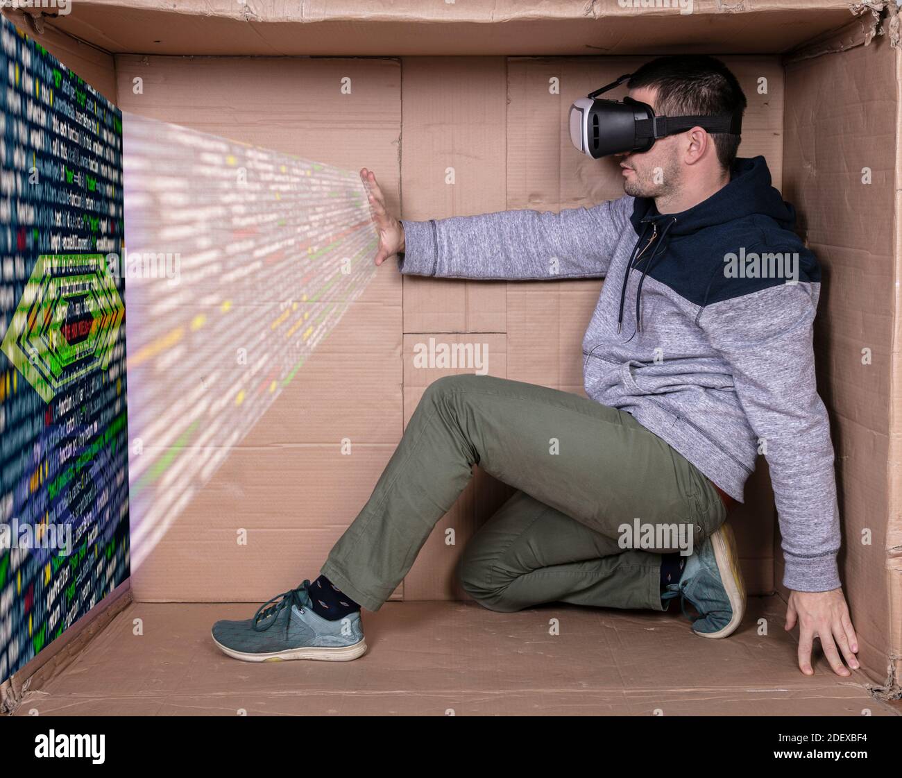 l'uomo con gli occhiali per la realtà virtuale si siede in un cartone e mostra il processo di programmazione Foto Stock