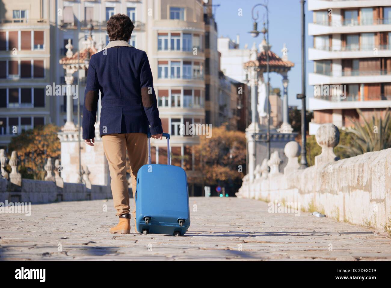 Un giovane irriconoscibile viaggia in Spagna durante una pandemia con una valigia blu mentre cammina attraverso il centro di una città per motivi di lavoro. Busi Foto Stock