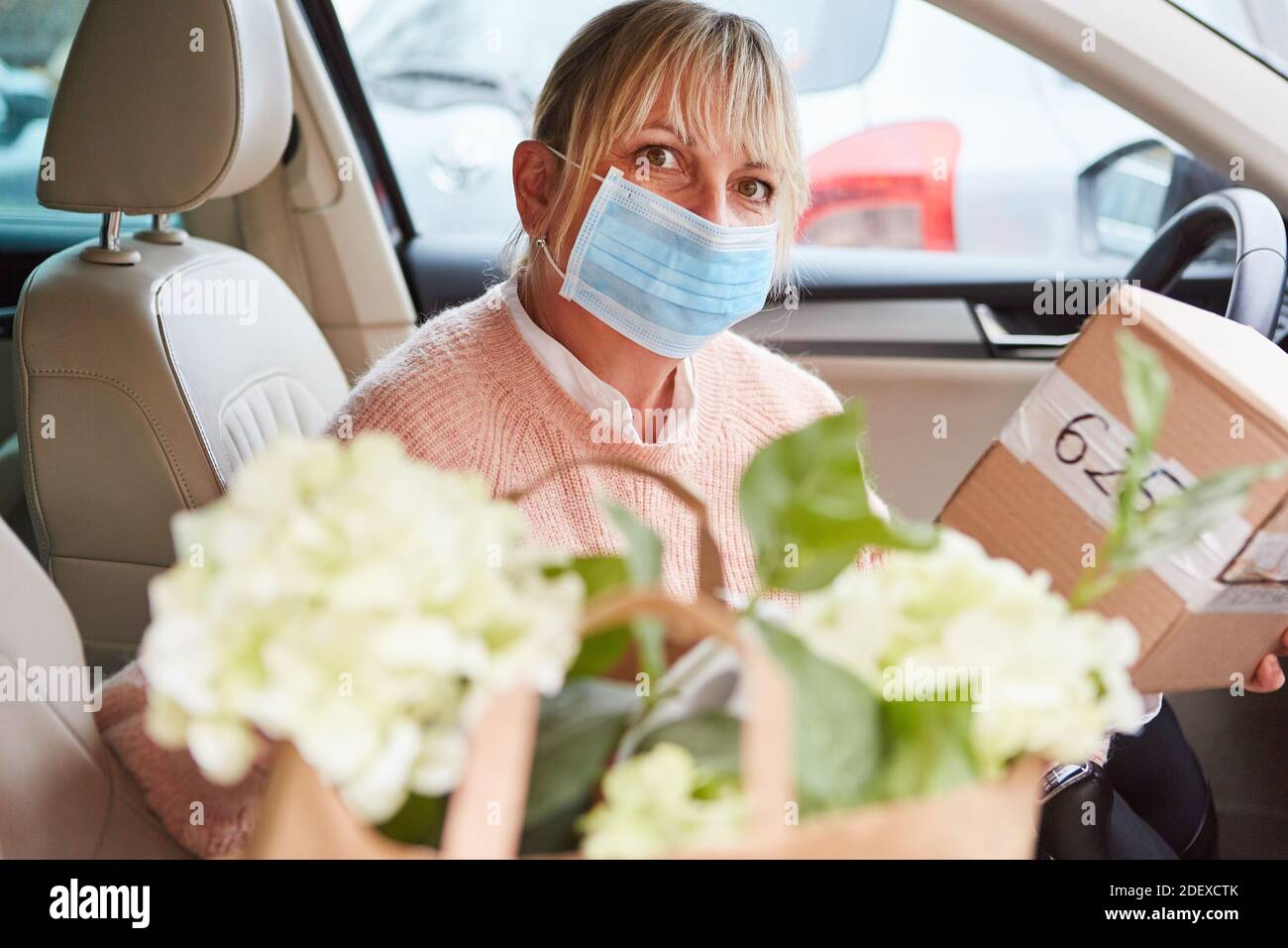 Donna con maschera in auto interni tiene pacchi di un servizio di consegna nelle sue mani Foto Stock