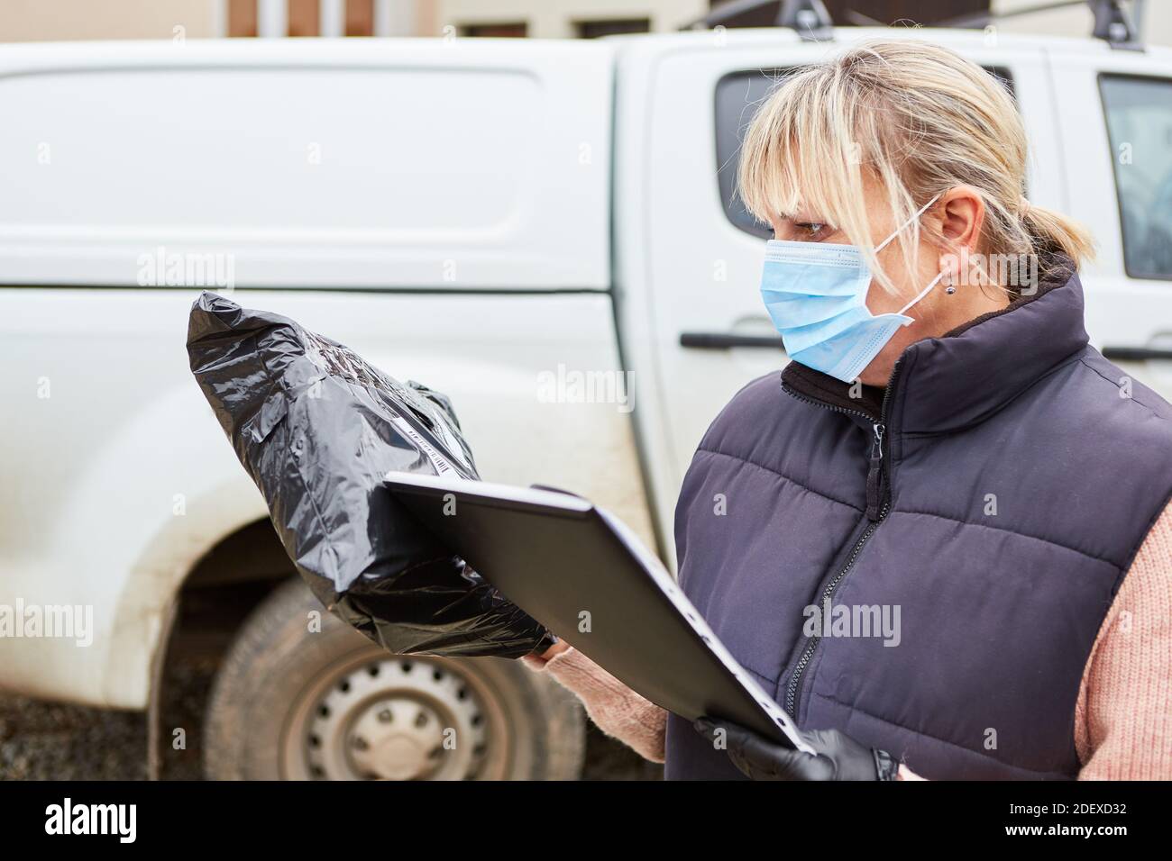 Il gestore pacchi con maschera facciale controlla la consegna con l'aiuto della lista alla consegna Foto Stock