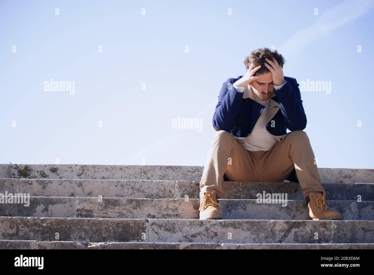 Panoramico giovane uomo di 24-30 anni seduto in strada frustrato dopo essere stato licenziato dal suo ultimo lavoro. L'uomo scontento perde il suo lavoro d'ufficio. Foto Stock