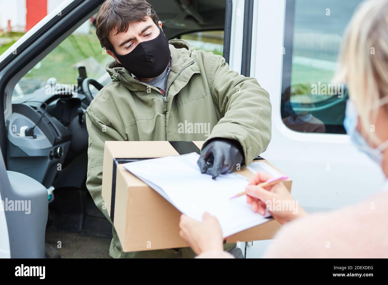 Il cliente firma una conferma di ricevimento del pacco dopo aver ricevuto la consegna con una maschera facciale dovuta a. Covid-19 Foto Stock