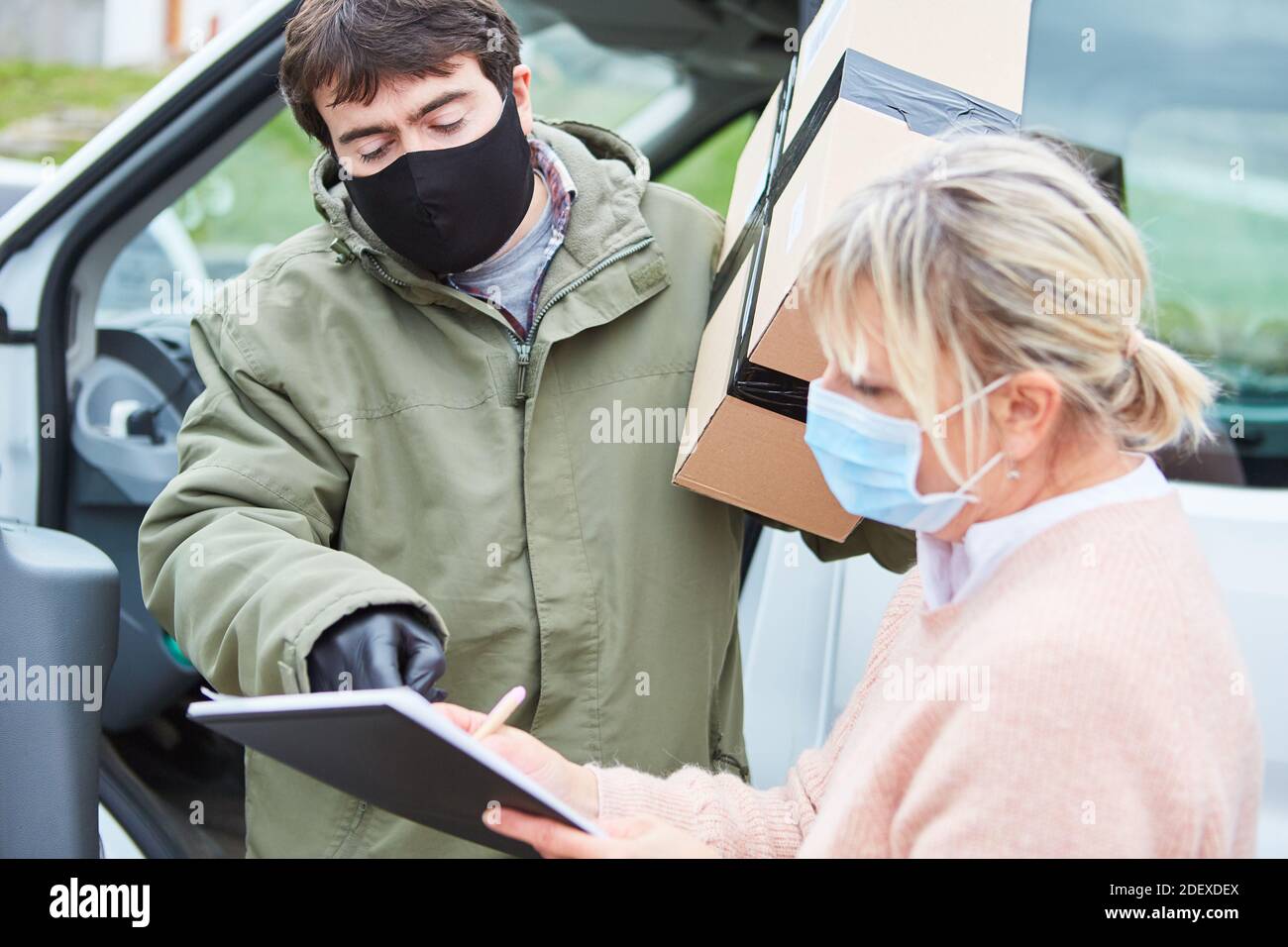 Il trasportatore di pacchi chiede la firma dopo la consegna del pacco con Maschera facciale dovuta a Covid-19 Foto Stock