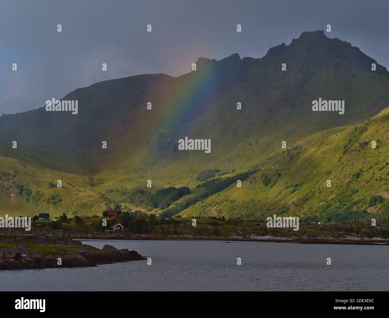 Incredibile arcobaleno colorato sopra caratteristiche case in legno con facciata dipinta di rosso in piccolo villaggio sulla costa dell'isola di Vestvågøy, Lofoten, Norvegia. Foto Stock