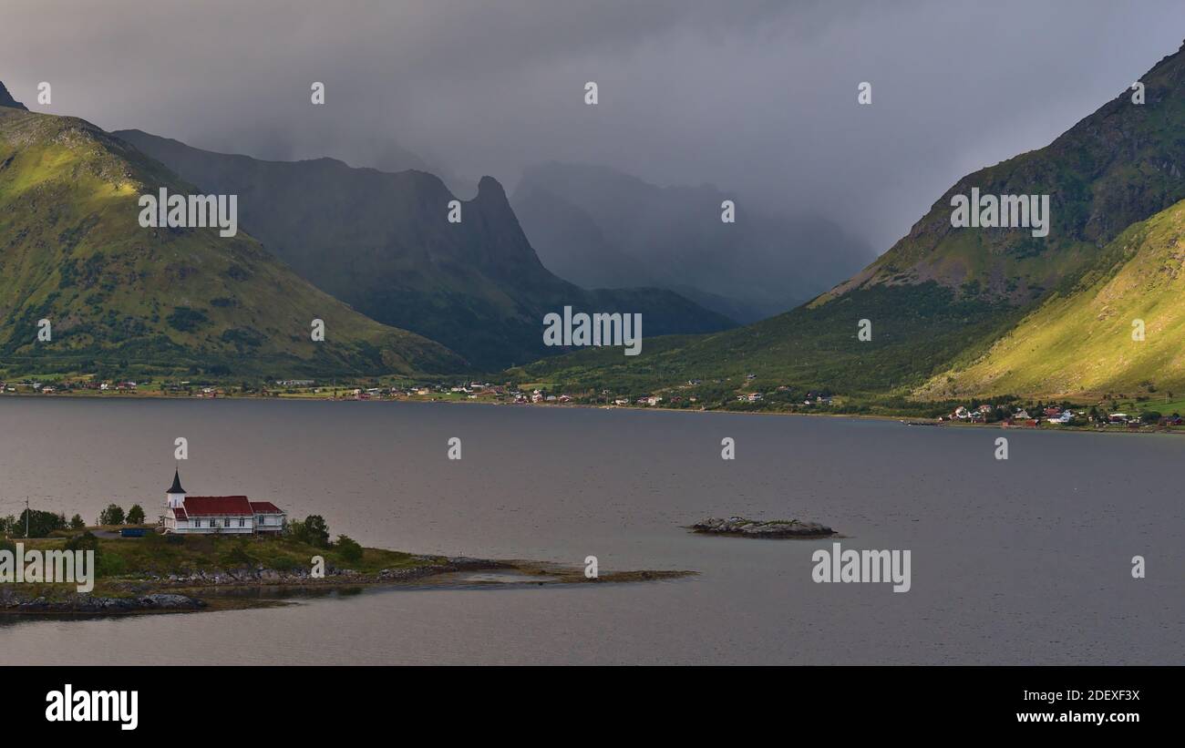 Bella vista della chiesa di Sildpollnes situata su una penisola in un fiordo sull'isola di Austvågøy, Lofoten, Norvegia con villaggio e sole che splende sulle montagne. Foto Stock