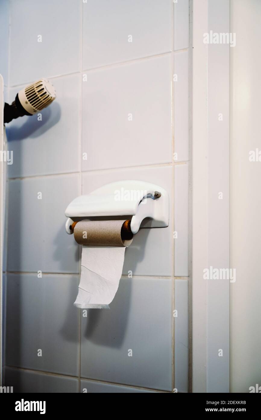 Un singolo foglio di carta igienica viene lasciato su un rotolo di carta igienica vuoto appeso su una parete piastrellata bianca in un bagno. Foto Stock