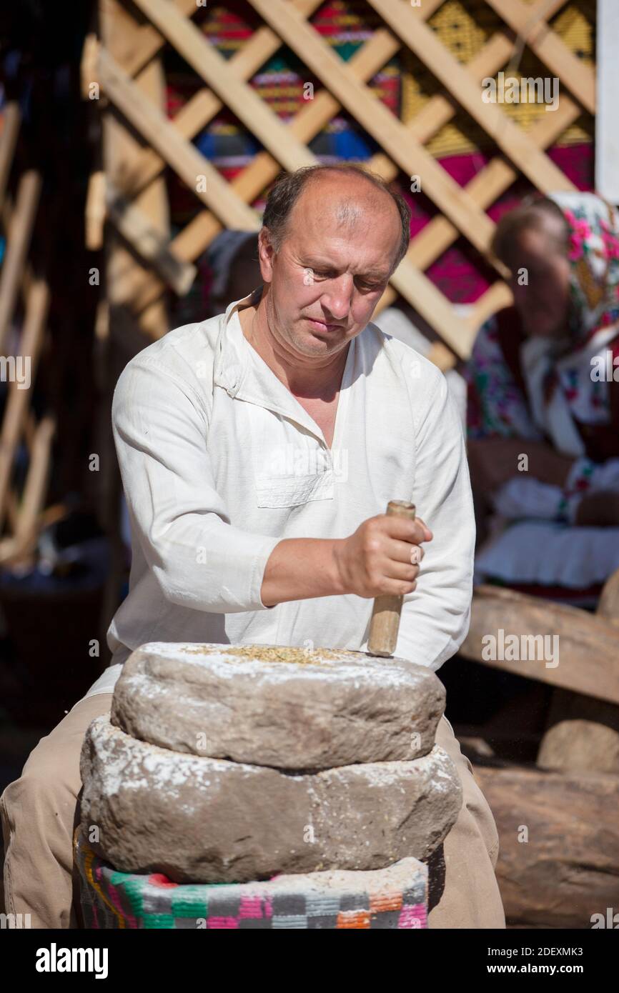 29 agosto 2020. Bielorussia, villaggio Lyaskovichi. Una vacanza di antichi mestieri. Un uomo macina la farina nel vecchio modo con l'aiuto di macine di pietra. Foto Stock