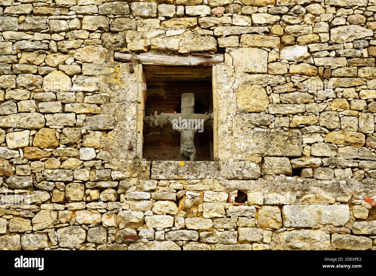 Gesù sulla croce, antico crocifisso, visibile dall'esterno, posto nella piccola finestra al centro della facciata medievale. Dordogna, a sud-ovest della Francia. Foto Stock